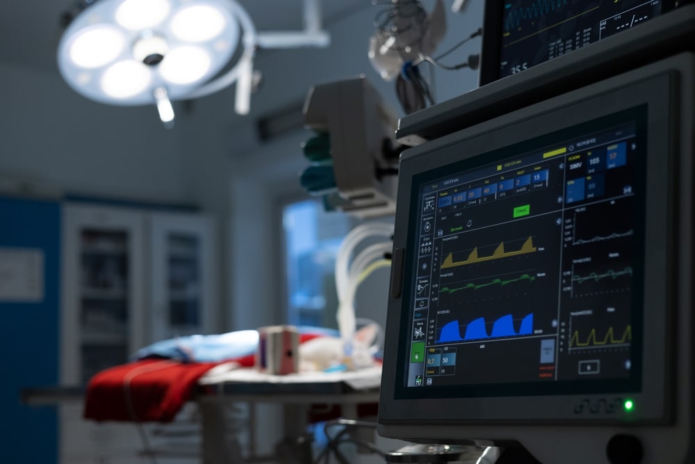Against the background of dark surgery in the light of a lamp a pet lies on the table and there is a monitor showing the life indicator After the operation the pet lies under the control of monitors.
